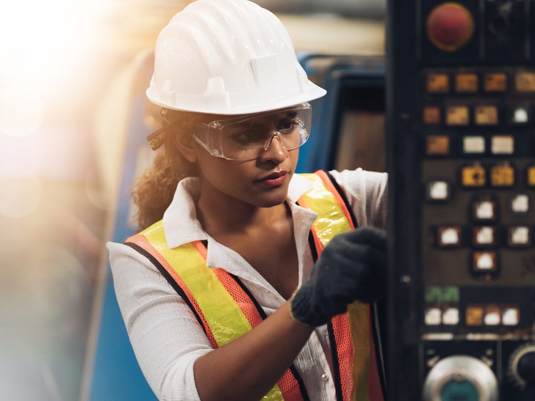 Photo of a woman with a hardhat and safety vest working on a control panel